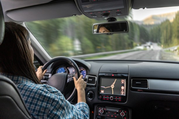 Woman driving a car on a winding road with a forest.