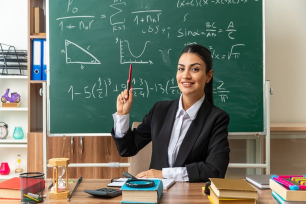 A smiling female teacher in a classroom with a blackboard.
