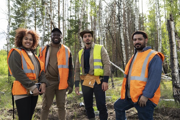 Four diverse people in safety vests in a forest.