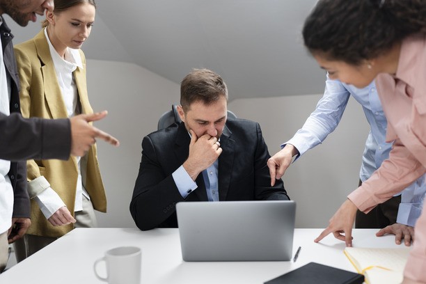 Stressed male worker surrounded by pointing colleagues